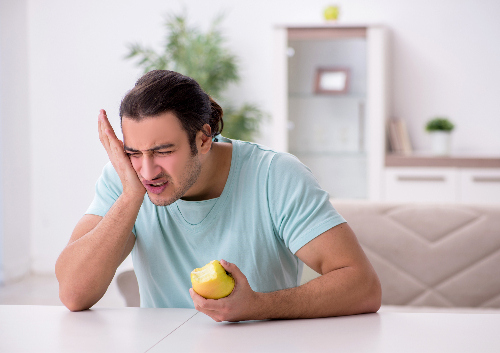 Man suffering from wisdom tooth pain whilst eating an apple.